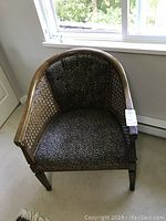 Front view of the cane chair showing its round back, cane sides, and leopard print upholstered seat and back.