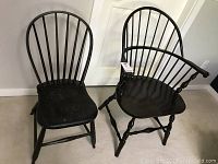 Pair of black wooden chairs against a white wall, showing front and side views with visible spindle backs and seats.