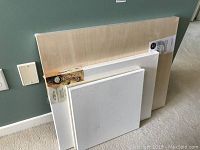 Four canvases including wooden cradled panel and wrapped canvases stacked against the wall