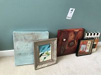 Group of five art prints including two framed, varied sizes, and styles against a wall.