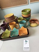 View of colorful ceramic dishware including mugs, small plates, star-shaped bowls on rectangular tray, and round bowls