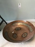 Front view of the large hammered copper bowl placed on the floor showing overall shape, size, and initial oxidation marks inside.