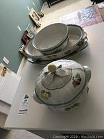 Photo showing stacked serving bowls, platters, and covered casserole dish with fruit and leaf patterns.