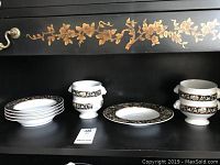 Set of flat rimmed bowls, pedestal soup bowls with lion's head handles, and a large pedestal bowl displayed on a shelf with a floral decal above.