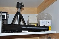 Black Bushnell 9 to 30 power 40mm zoom spotting scope horizontally placed on a shelf near a Bushnell tripod.