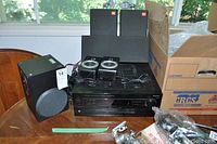 Receiver and speakers arranged on a wooden table with boxes in background. Shows receiver front with speakers surrounding it to display lot contents.