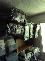 Five comforters packaged inside individual clear plastic zippered bags stacked on shelf.