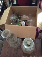 Five oil lamps displayed, two large clear glass lamps with hexagonal bases and chimneys, box with lamp parts, general wear visible