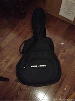 Soft black nylon carrying case with 'World of Music' in white text on the front pocket, lying on wooden floor.