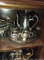 Top shelf showing silverplate coffee pot, sugar bowl, creamer, and a decorative tray
