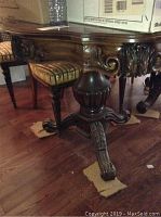 Close-up of carved wooden pedestal leg of table showing detailed scroll and leaf designs with claw-foot base.