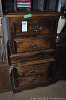 Two dark wood end tables stacked, showing three drawers each with metal handles and visible wood grain and some scratches.