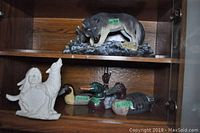 Shelf with large wolf figurine on top shelf and smaller figurines including white Native American and wolf sculpture and wooden duck decoys below
