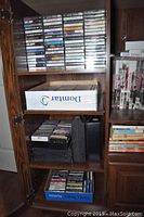 Wooden cabinet shelves filled with many musical cassette tapes stacked and organized in boxes and vertically.