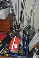 Multiple fishing rods with reels leaning against door and stored in blue bin