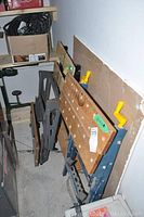 Three Mastercraft folding work benches stored against wall, showing wooden tops with holes and frames with yellow handles.