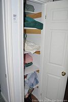 Closet door open showing shelves with folded linens and towels in various colors and textures.