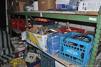 View of metal shelves holding assorted hardware including boxes, milk crates filled with items, extension cords, tools, and hardware supplies.