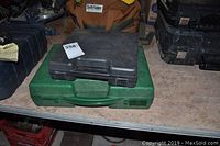Two stacked tool cases on a table — a black plastic case on top of a green plastic case.