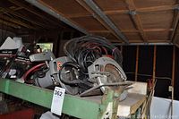 Wide view showing two circular saws and a red air tank with coiled hoses on a green metal shelf.