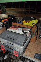 Weller soldering gun box placed on top of a closed black and gray plastic toolbox with an orange and black tool bag behind.