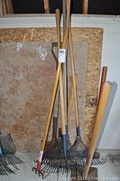 Photo showing the full set of garden tools leaning against a wall, including rakes, shovel, and tamper with wooden handles.