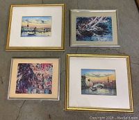 Four framed art pieces displayed on floor showing variety of scenes and framing styles