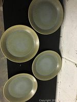 Four round ceramic plates with a blue-green matte glaze and textured edges, shown on black surface.