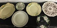 Set of six vintage plates with various floral and patterned designs displayed on a black surface