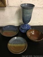 Overall view of the set showing one tall vase with blue and green glazing and three shallow bowls with various earth tone glazes