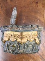 Front view of hand carved wooden plaque showing two bearded faces under rough bark edge