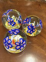 Three clear glass paperweights on wooden surface, showing blue floral designs inside each sphere.