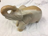 Front and side view of carved stone elephant sculpture with curled trunk and smooth, natural stone finish.