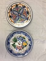 Two hand-painted Spanish ceramic plates placed on a white cloth background showing colorful designs and good condition.