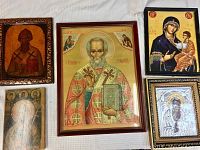 Five Greek Orthodox religious art icons shown together on a cloth surface, varying sizes and frames visible.