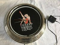 Full clock showing chrome frame, black dial with Betty Boop cartoon graphic and text. Power adapter shown next to clock.