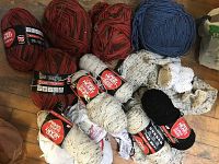 Overview of yarn packages and loose yarn on floor including red variegated and cream speckled skeins.