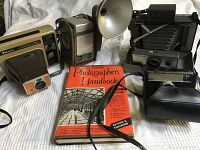 Four vintage cameras and one hardcover photography handbook shown together, displayed on a white surface.