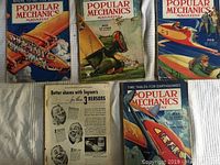 Five vintage Popular Mechanics magazines displayed, covers show aircraft and detailed cutaway drawings from issues spanning 1934 to 1935.