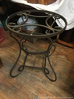 Side view of metal table base showing curved scroll design on legs and around the top