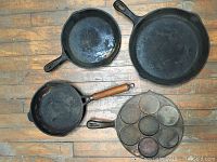 Overview of four cast iron pans shown on wooden floor.