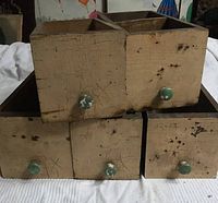 Five vintage wooden drawers stacked showing front view with paint cracking and blue-green knobs with paint chipping.