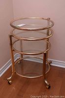 Full view of the three level rolling stand showing metal frame with circular glass shelves stacked and aligned.