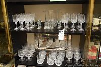 Two shelves of glassware showing Cristal d'Arques Paris Longchamp crystal wine glasses, tumblers, snifters, clear cut diamond patterned ice bucket and additional smaller liquor and spirit glasses.