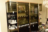 Front view of entire cabinet showing smoked glass cupboards and shelving containing dish sets and glassware.