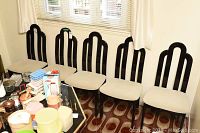 Four black wooden dining chairs with cream upholstered seats arranged in a row in front of a window.