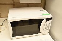 Front view of white Danby microwave oven with power cord visible, labeled with model and dimensions sticker.