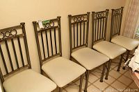Side view of six metal frame dining chairs with cream colored cushioned seats lined up together.