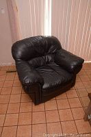 Front side view of black leather armchair showing the cushioned backrest, padded armrests, and seat with leather upholstery.