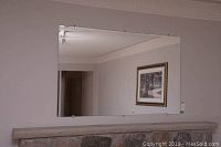Full view of large rectangular beveled wall mirror mounted on a wall above a fireplace mantel, showing the entire reflective surface and overall size.